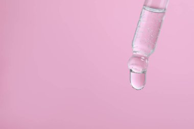 Pembe arka plandaki pipetten serum damlıyor, yakın plan. Metin için boşluk