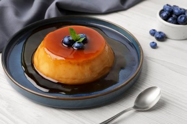 Plate of delicious caramel pudding with blueberries and mint served on white wooden table clipart