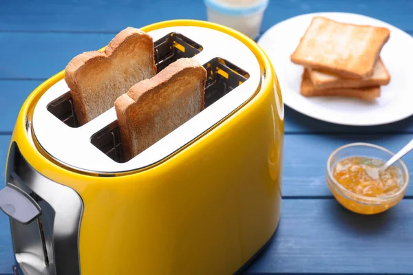 烤面包和果酱放在蓝色木制桌子上的黄色烤面包机 特写镜头 — 图库照片