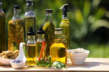 Ahşap masadaki farklı yemek yağları ve malzemeler bulanık yeşil arka planda.