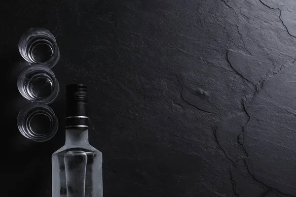 ウォッカのボトルと黒いテーブルの上のショットグラス フラットレイ テキストのスペース — ストック写真