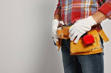 Professional builder with tool belt on light background, closeup. Space for text