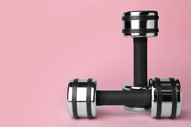 Açık pembe arka planda iki metal dambıl