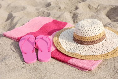 Hasır şapkalı plaj havlusu ve kumdaki terlikler.