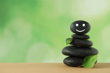 Üzerinde mutlu yüz ve yeşil yapraklar çizilmiş taşlar yığını bulanık arka planda, yazı için yer var. Zen kavramı