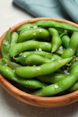Bir kase yeşil edamame fasulyesi kabuklarda açık gri masada tuz, yakın plan.