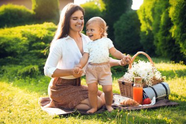 Mother with her baby daughter having picnic in garden on sunny day