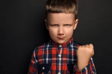 Angry little boy on black background. Aggressive behavior