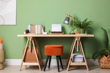 Writer's workplace with typewriter on wooden desk near pale green wall in room