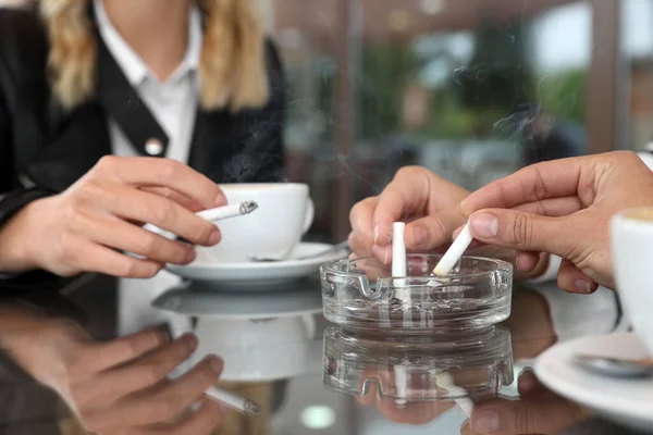 stock image Women putting out cigarettes in ashtray at table, closeup