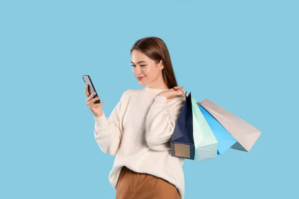 Schöne Junge Frau Mit Einkaufstaschen Die Ihr Smartphone Auf Hellblauem — Stockfoto
