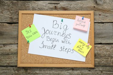 Corkboard with motivational quotes on wooden table, top view clipart