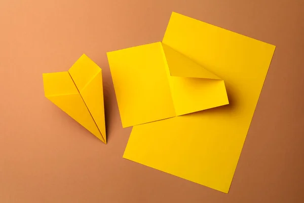Handmade yellow plane and pieces of paper on brown background, flat lay