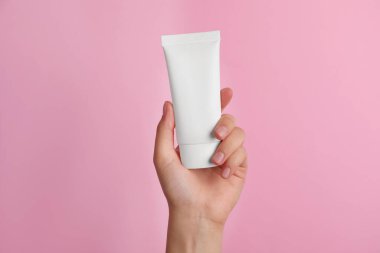 Pembe arka planda yüz kremi tüpü tutan kadın, yakın plan.