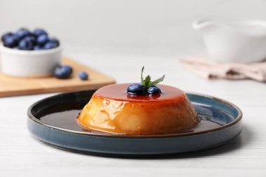Lezzetli karamelli puding, yaban mersinli ve nane şekerli beyaz ahşap masa.