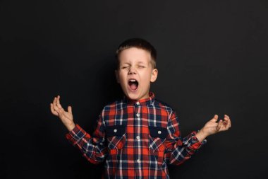 Angry little boy screaming on black background. Aggressive behavior