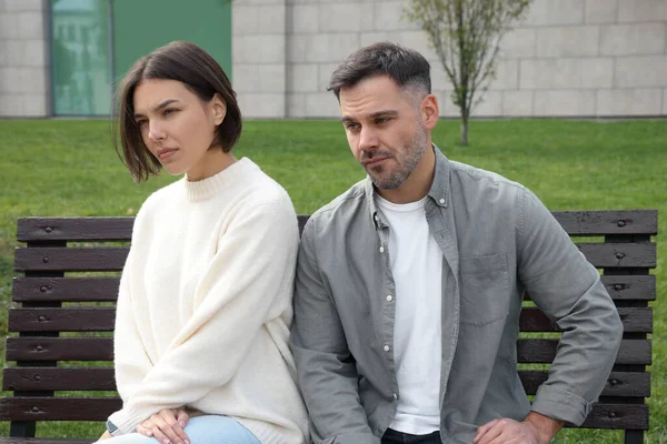 Unhappy couple sitting on bench outdoors. Relationship problems