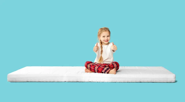 Kleines Mädchen Sitzt Auf Matratze Und Zeigt Daumen Nach Oben — Stockfoto