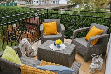 Renkli yastıklar, yumuşak battaniye ve sarı kasımpatı çiçekleri açık havadaki bahçe mobilyalarında.