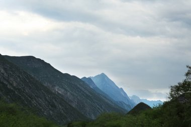 Açık havada kasvetli gökyüzü altında yüksek dağları olan resim gibi bir manzara.