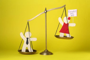 Cinsiyet farkı. Erkek ve kadının ahşap figürleri sarı arka planda.