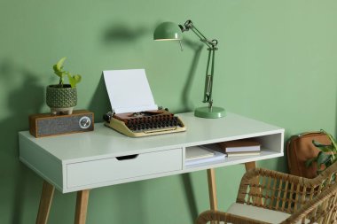Writer's workplace with typewriter on wooden desk near pale green wall in room