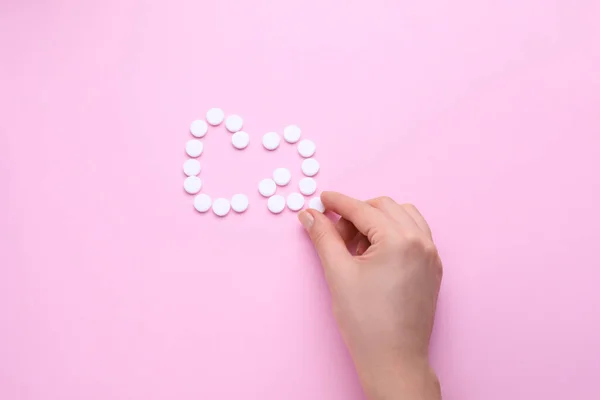 Woman making calcium symbol with white pills on pink background, top view