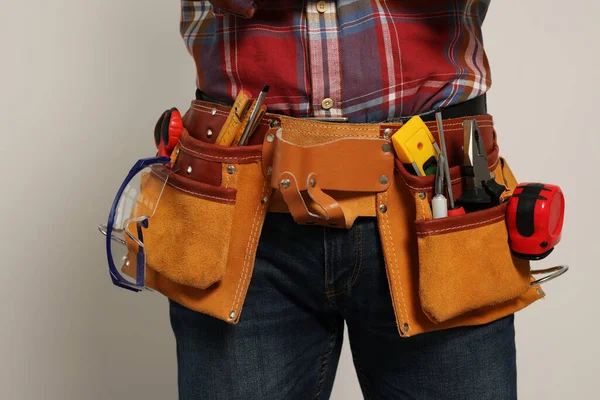 Professional builder with tool belt on light background, closeup