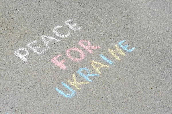 Words Peace For Ukraine written with colorful chalks on asphalt outdoors