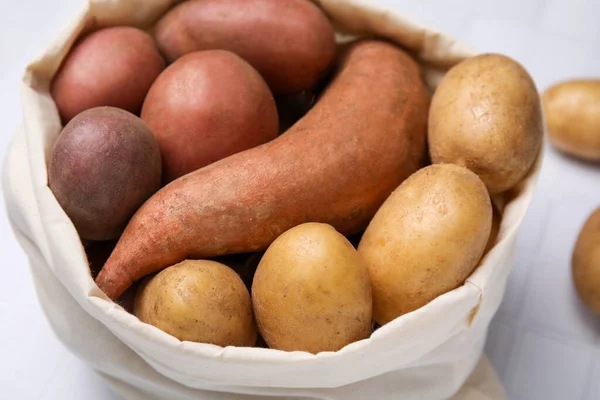Different types of fresh potatoes in bag on white table, closeup