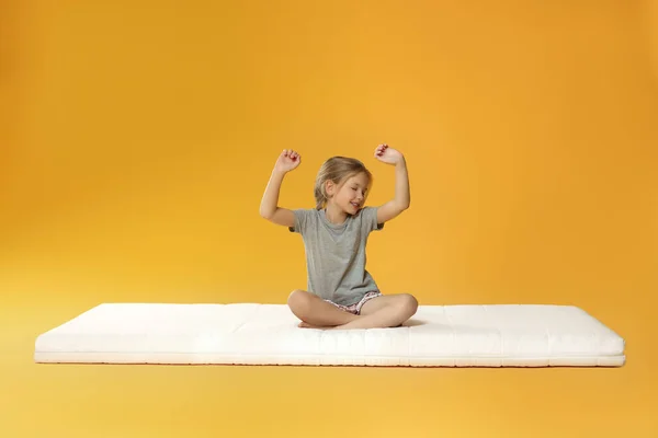 Kleines Mädchen Wacht Auf Matratze Vor Orangefarbenem Hintergrund Auf — Stockfoto