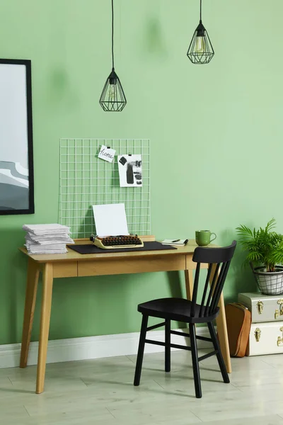 Typewriter, stack of papers and mood board on wooden table near pale green wall. Writer\'s workplace