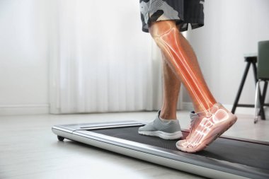 Digital composite of highlighted bones and man training on walking treadmill at home, closeup clipart