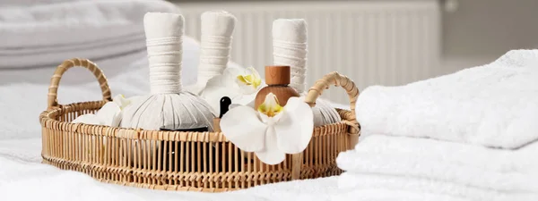 Wicker tray with herbal bags and other spa products on white bath towel. Banner design
