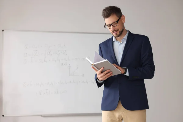 Teacher with book at whiteboard in classroom during math lesson