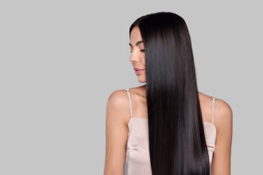 Açık gri arka planda sağlıklı, güçlü saçları olan güzel genç bir kadının portresi.