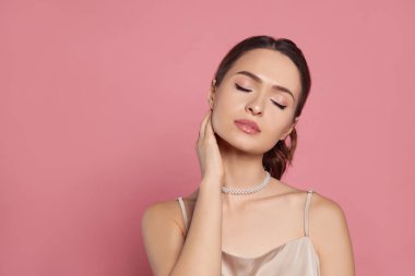 Pembe arka planda zarif inci kolye takan genç bir kadın.