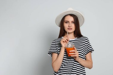Açık gri arka planda plastik bardak meyve suyu olan güzel genç bir kadın.