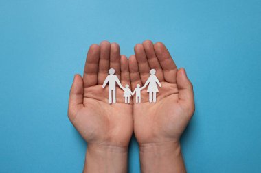 Elinde kağıt aile figürleri olan açık mavi arka planda bir adam. Sigorta konsepti