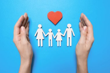 Açık mavi arka planda aile figürlerini koruyan bir kadın. Sigorta konsepti