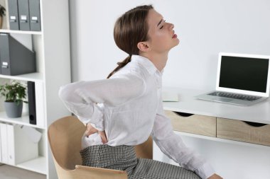 Ofiste otururken sırt ağrısı çeken bir kadın. Skolyoz belirtileri