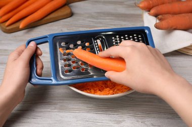 Woman grating fresh carrot at wooden table, closeup clipart