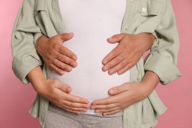 Man hugging his pregnant wife on pink background, closeup