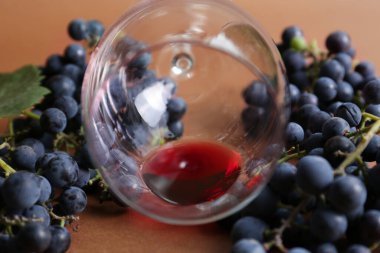 Kahverengi arka planda kırmızı şarap ve üzümlü ters çevrilmiş cam, yakın plan.