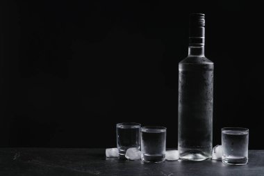 Siyah arka planda buzlu bir şişe votka ve shot bardakları. Metin için boşluk