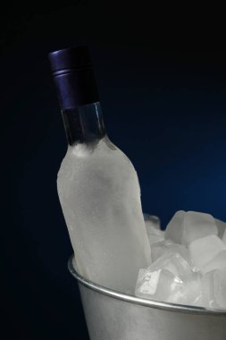 Bir şişe votka metal kovada, buzlu ve siyah arka planda.