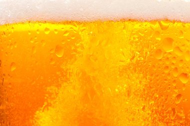 Glass of tasty cold beer with foam and condensation drops as background, closeup