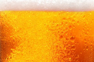 Glass of tasty cold beer with foam and condensation drops as background, closeup