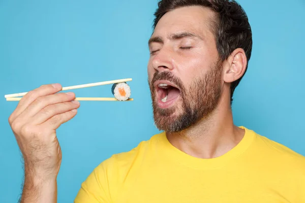 Schöner Mann Isst Sushi Rolle Mit Stäbchen Auf Hellblauem Hintergrund — Stockfoto