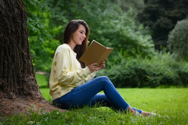 年轻女子在公园的一棵树旁看书 — 图库照片